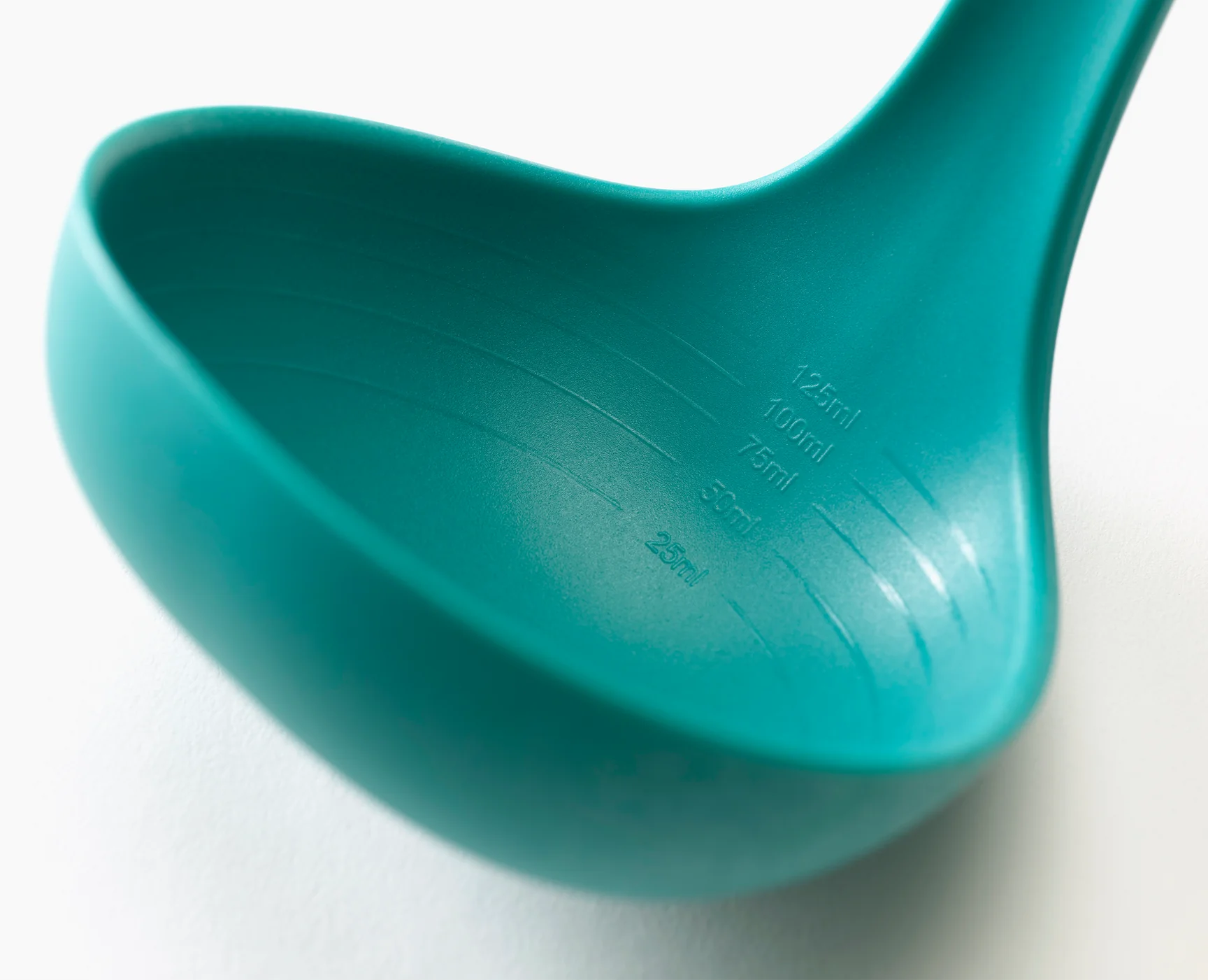 Close-up of teal silicone utensil head with embossed measurements and brand markings.