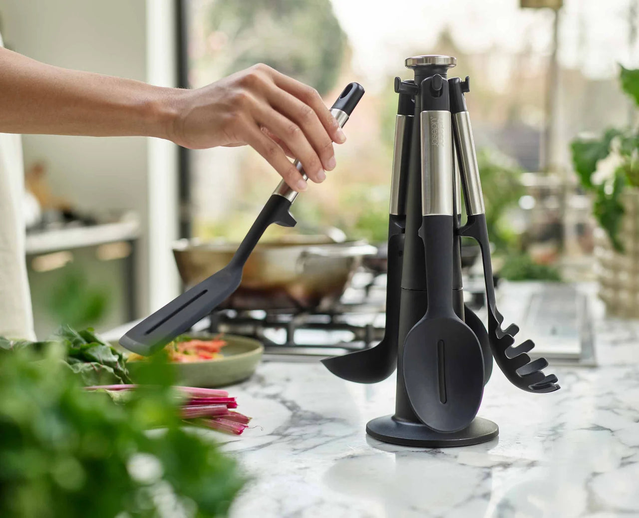 Slotted turner in hand over a pan, with black-and-stainless utensil stand