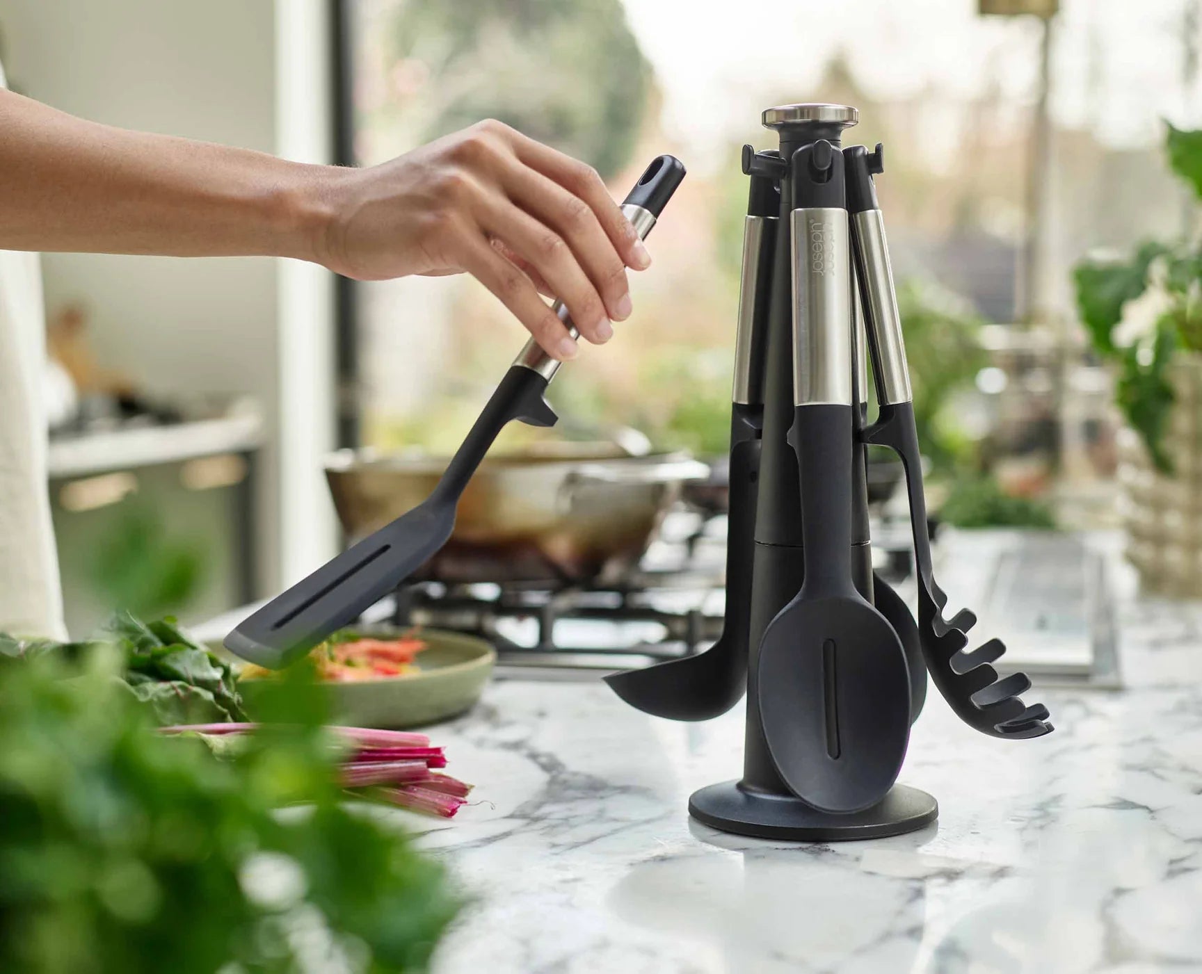 Slotted turner in hand over a pan, with black-and-stainless utensil stand
