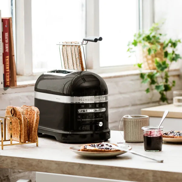 Black toaster on a kitchen counter with toast, a plate of food, and a cup.