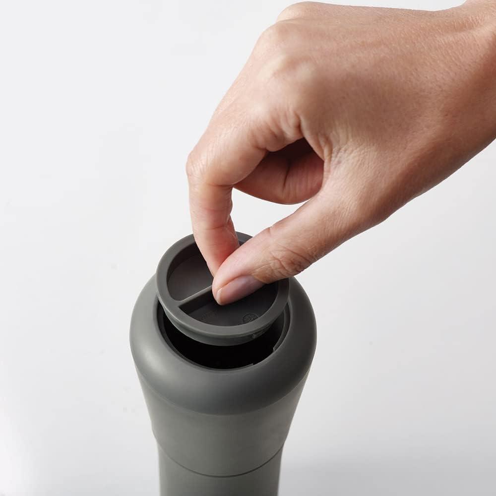 Dark grey non-spill salt and pepper mill with top cover open, hand adjusting