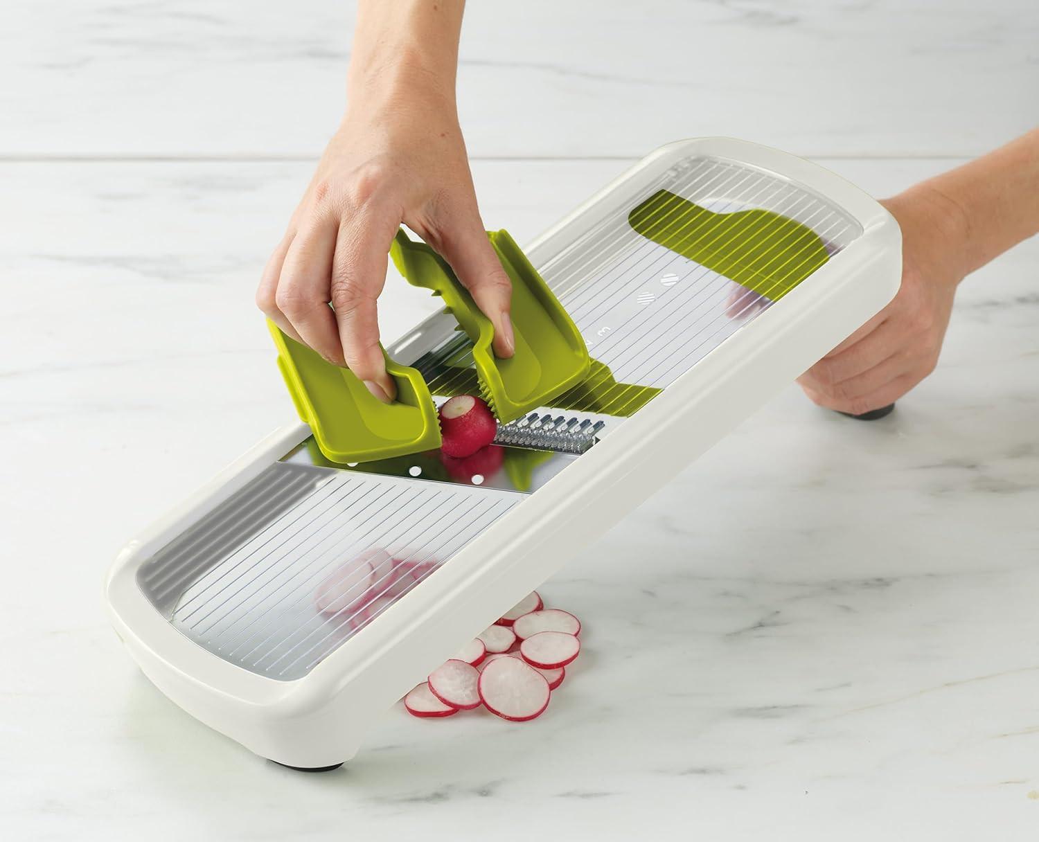 White mandoline slicer with green hand guard and sliced red vegetable pieces