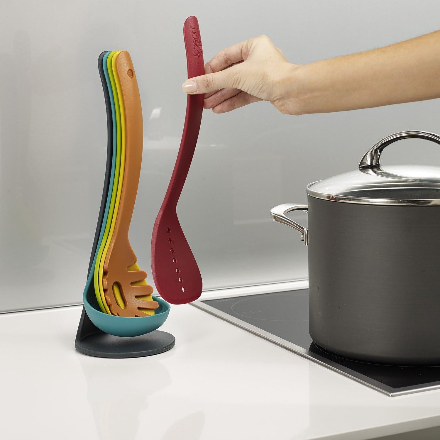 Hand placing a multicolour silicone utensil onto a teal magnetic stand next to a pot.