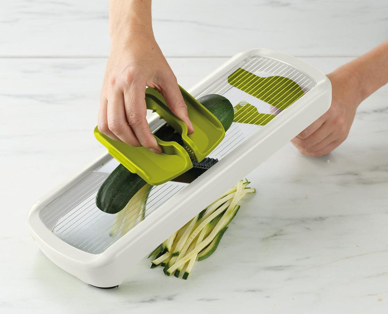 White kitchen mandoline slicer with green hand guard slicing green vegetables