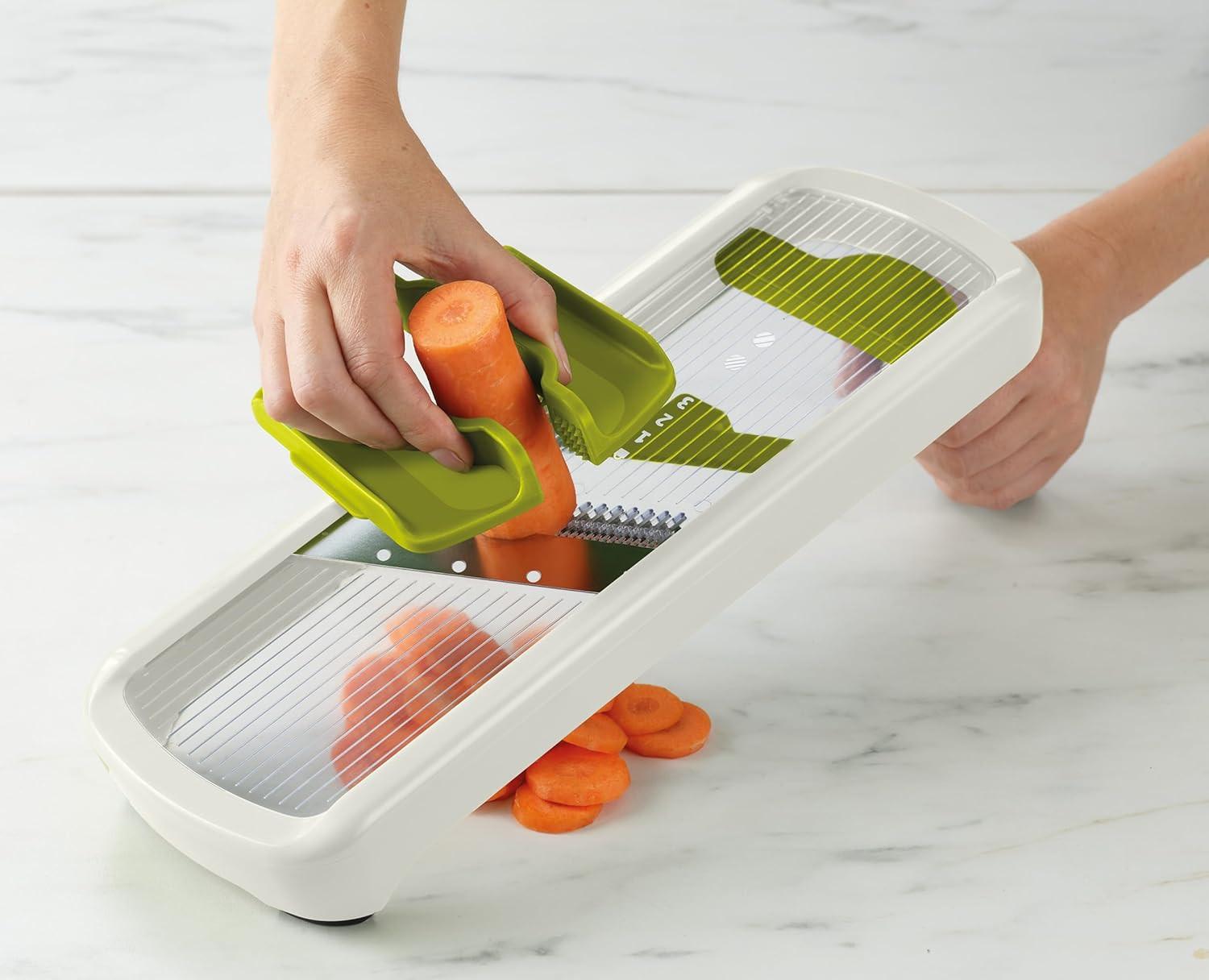 White mandoline slicer with green hand guard holding an orange vegetable
