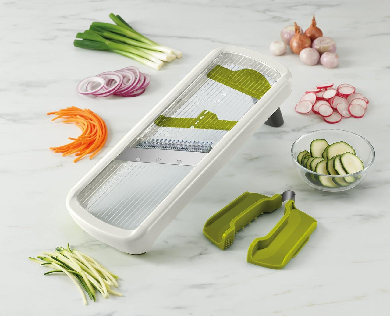 White mandoline slicer kit with green blade holders and assorted sliced vegetables