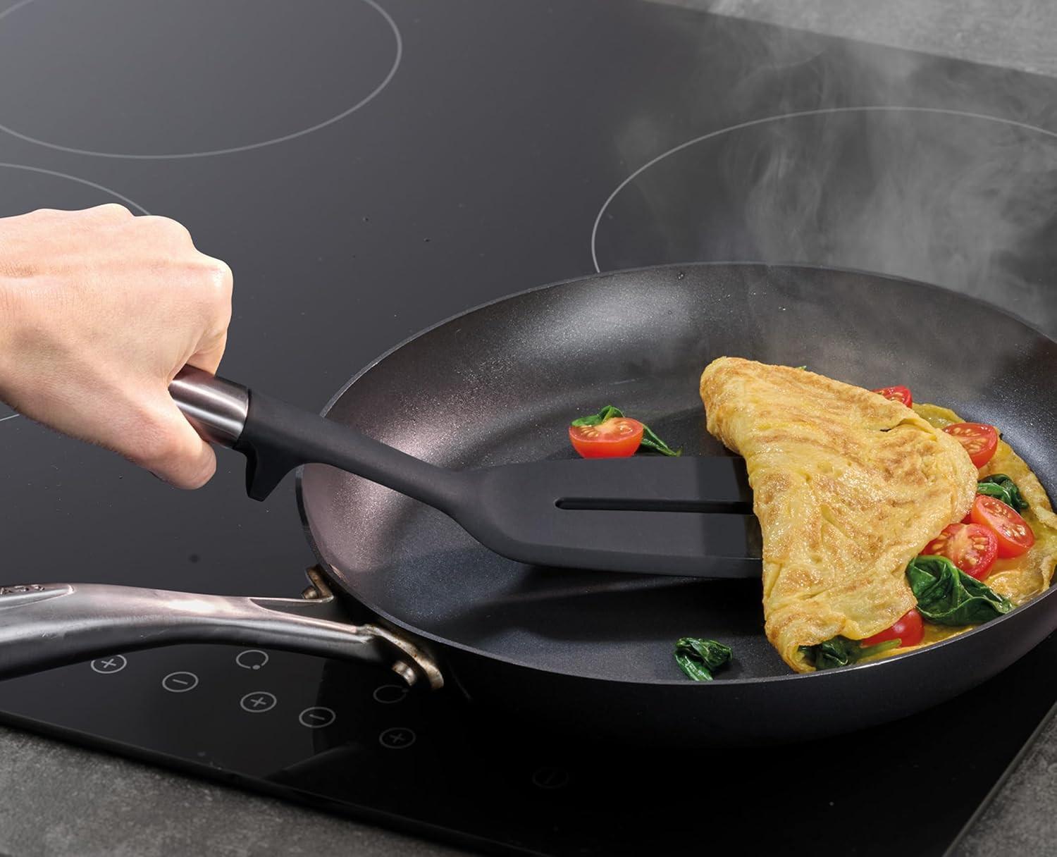 Black silicone kitchen spatula in a nonstick frying pan with vegetables