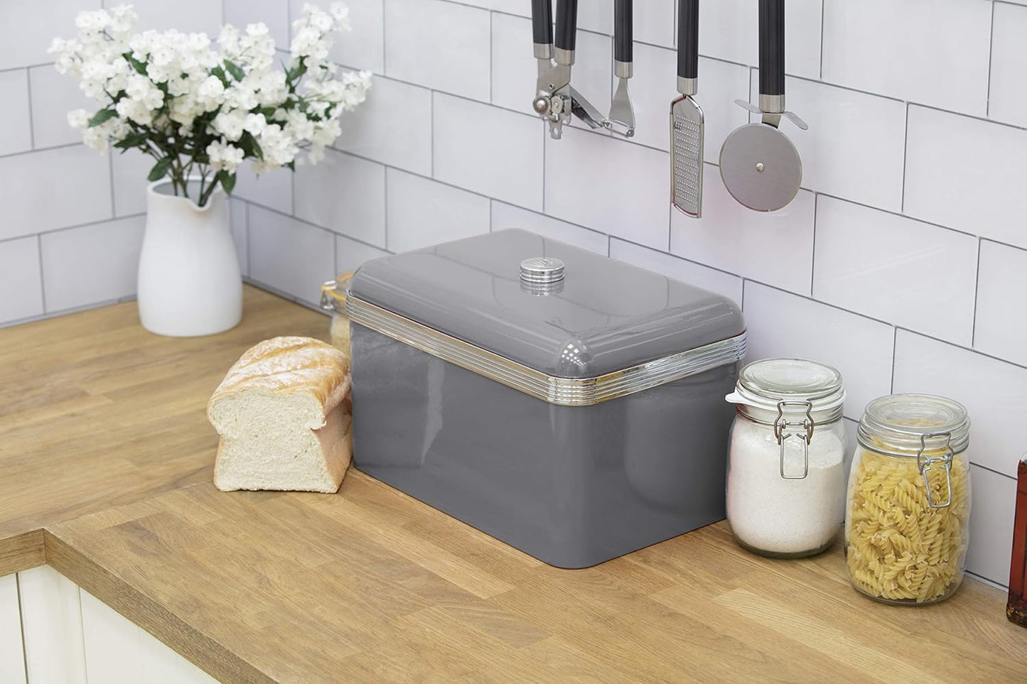 Grey retro bread bin with silver ribbed trim beside kitchen jars and bread pieces