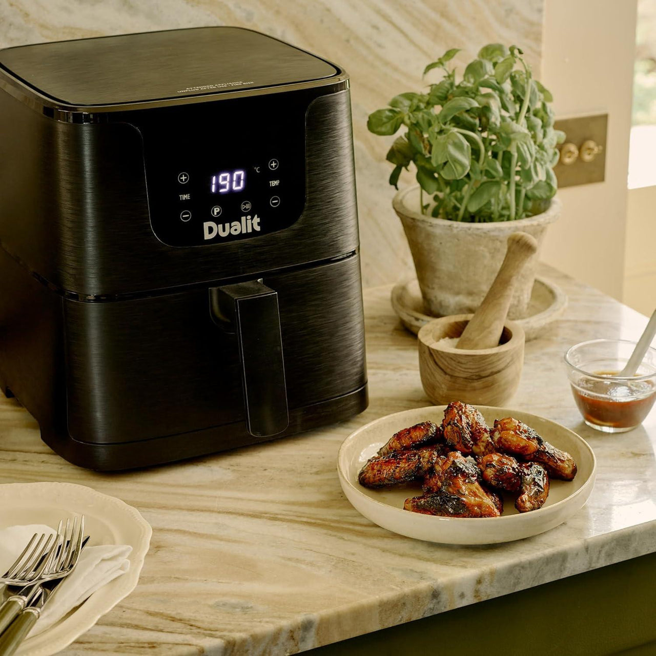Black Dualit air fryer next to plate of cooked wings on countertop.