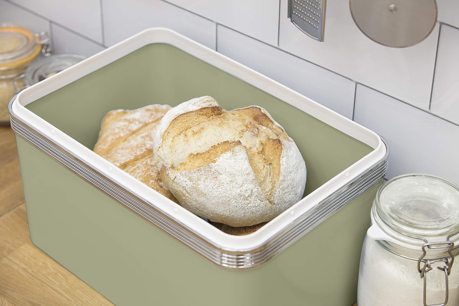 Green bread bin filled with sliced loaf, silver-trimmed lid and side canister jars