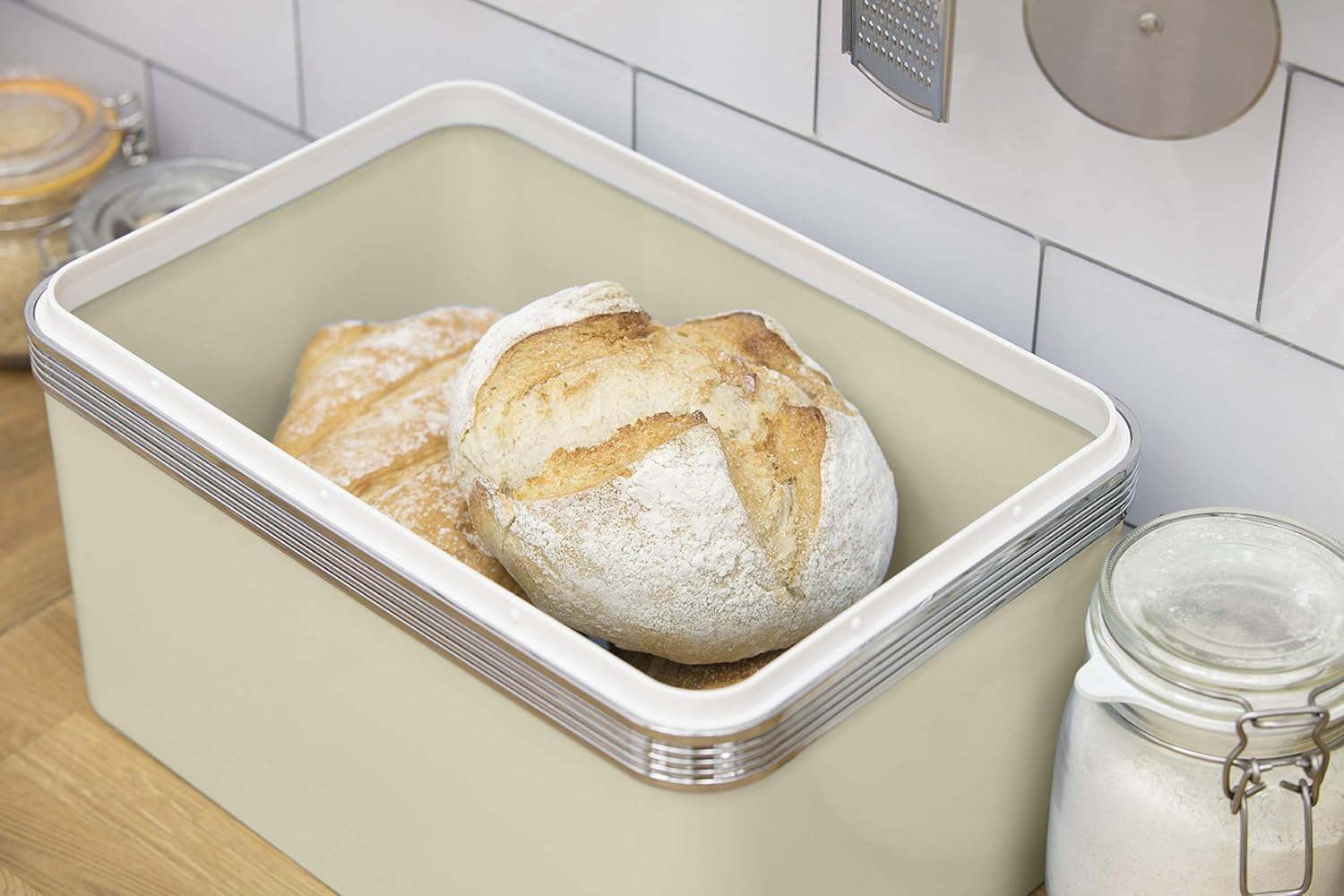 Cream retro bread bin with open lid holding a round loaf of bread.