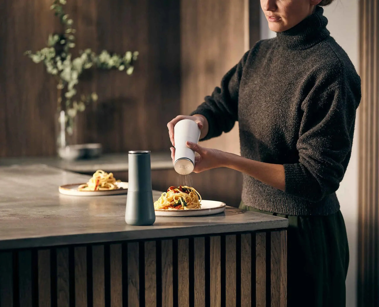 Non-spill salt and pepper mill in use, hand turning stainless-topped dark grey mill