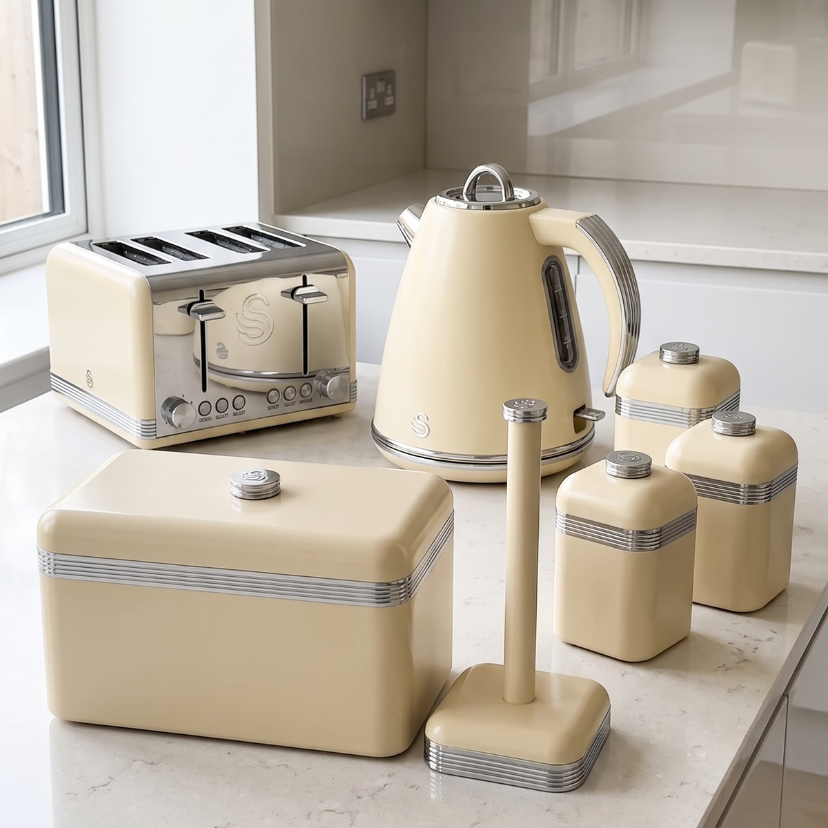 A coordinated cream-colored retro kitchen appliance set arranged on a light marble countertop in a modern kitchen. The set includes a four-slot toaster, a kettle, several canisters, a bread bin, and a stand.