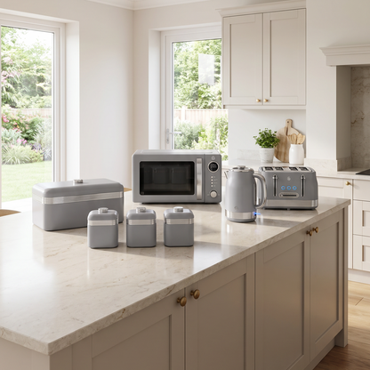 A modern kitchen island with cream shaker-style cabinets and a light marble countertop, styled with grey kitchen accessories including a microwave, toaster, kettle, and canisters. The room features white walls, recessed lighting, and wood flooring.
