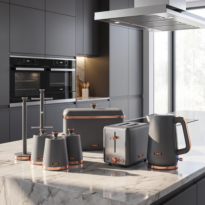 A modern kitchen island setup featuring a coordinated set of dark gray countertop appliances with copper accents, including a kettle, toaster, coffee maker, and canisters, set against dark gray cabinetry and a white marble island.