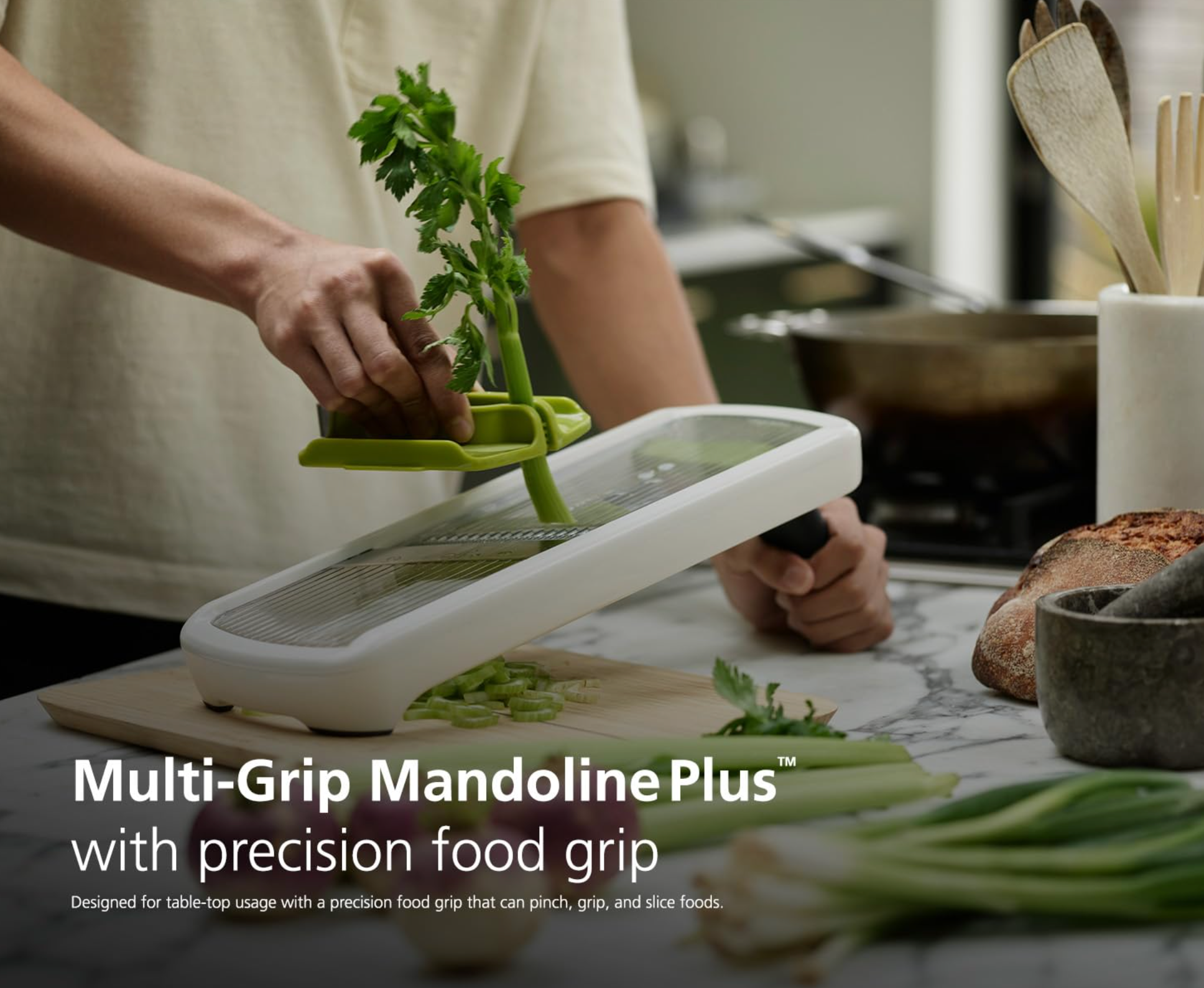 Kitchen mandoline on countertop with green guard and leafy herbs being sliced
