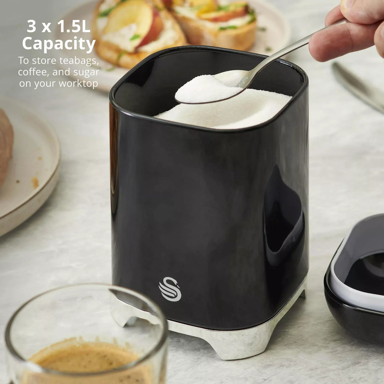 Black canister with glossy lid open; spoon holding white sugar inside storage