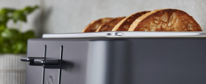 Matt black toaster partially in use, showing a slice in the upper warming slots.