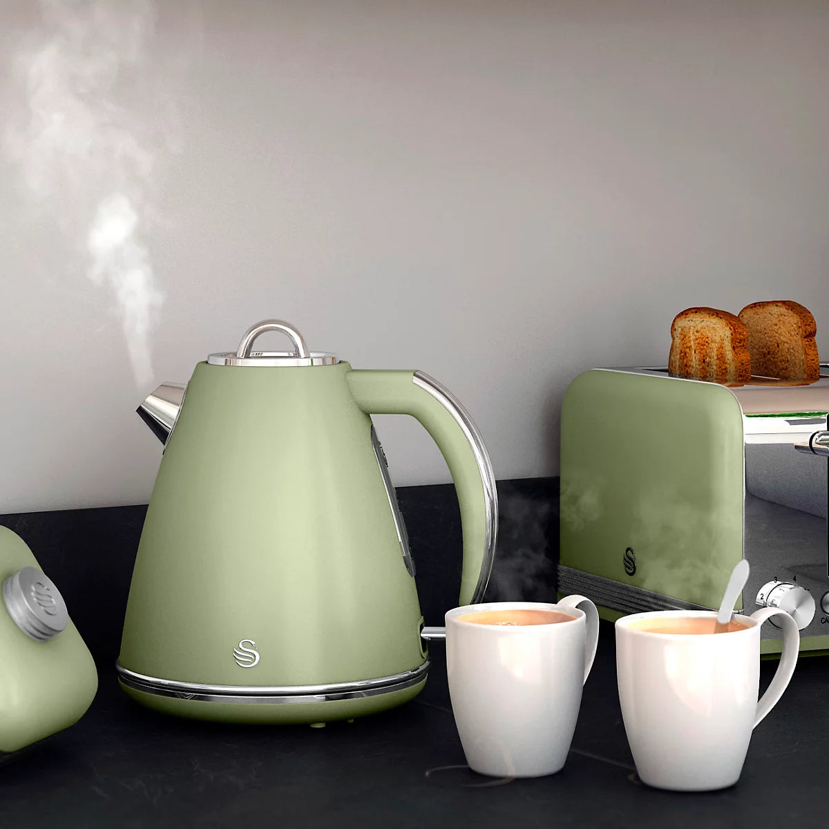 Green kettle with two white mugs on a kitchen counter, with toast in the background.