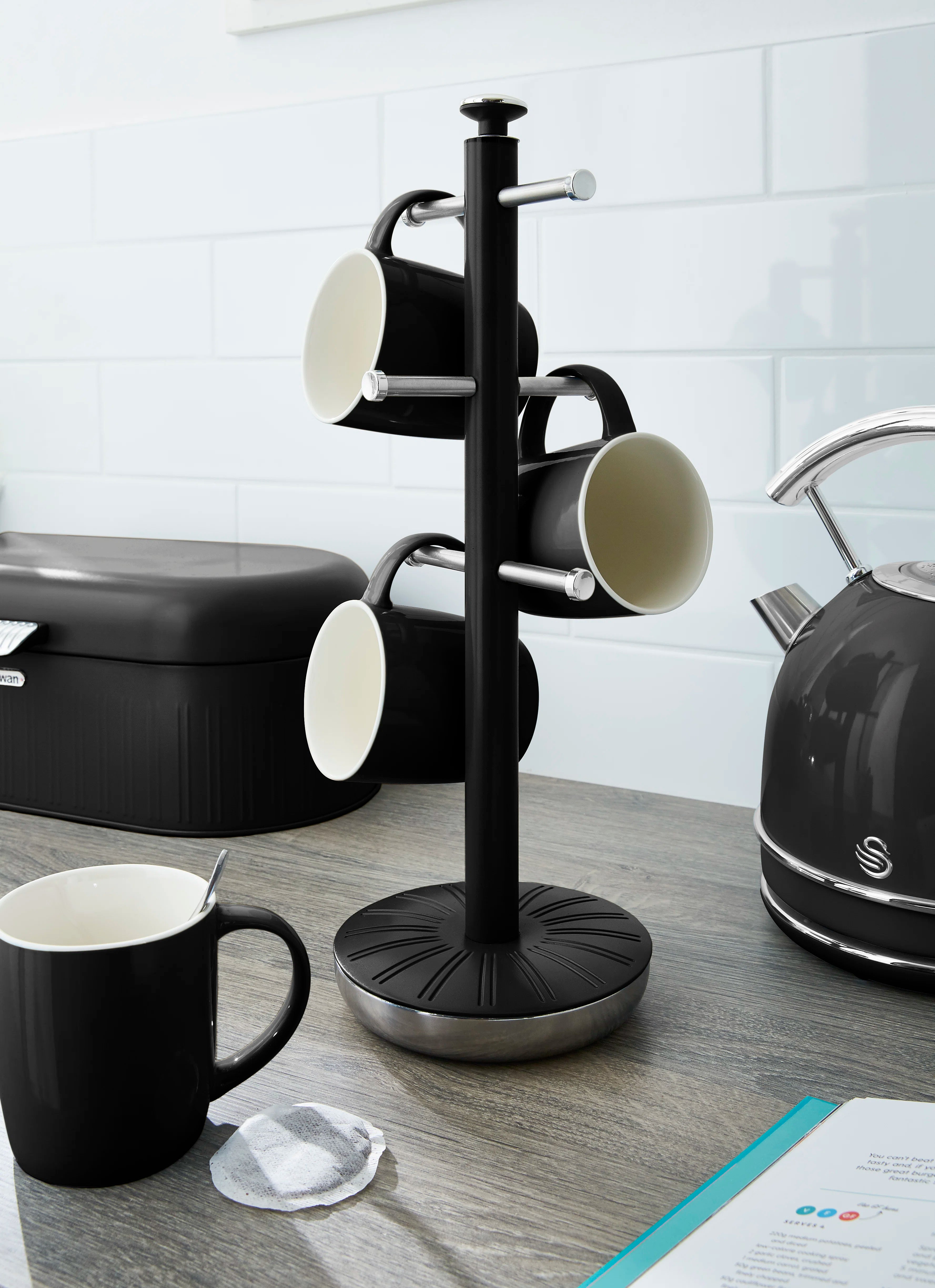 Black mug tree with multiple mugs on hooks and round base